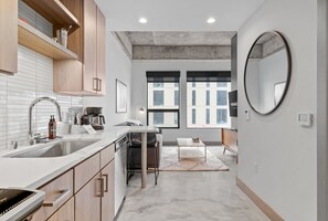A modern kitchen with a large sink, wooden cabinets, and a marble countertop. There is a dining area with a table and chairs, and a large mirror on the wall. - Sable 203 - Alcove (Minneapolis)