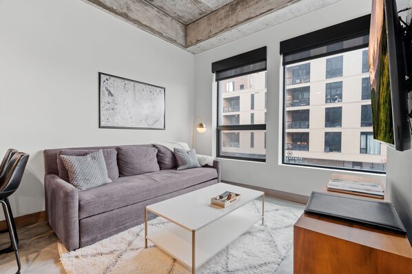 A modern living room with a grey sofa, a white coffee table, and a large window with a view of buildings. - Sable 203 - Alcove (Minneapolis)