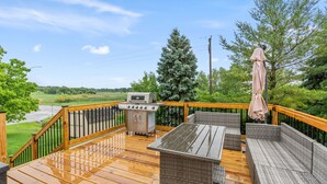 Une terrasse en bois, meublée de meubles en osier, avec un barbecue et une vue sur un paysage verdoyant.
