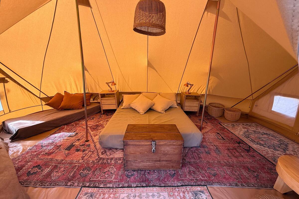 A tent with a bed, two nightstands, a hanging light, and a woven basket.