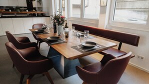 A modern dining area with a wooden table, dark brown chairs, and a bench. There are wine glasses, bottles, and a vase with flowers on the table. - Goldstadtloft (Pforzheim)
