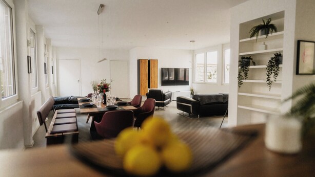 A modern living room with a dining area, a sofa, a TV, and a bookshelf with plants. - Goldstadtloft (Pforzheim)