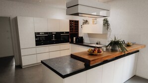 A modern kitchen with white cabinetry, a black countertop, and a built-in oven. - Goldstadtloft (Pforzheim)