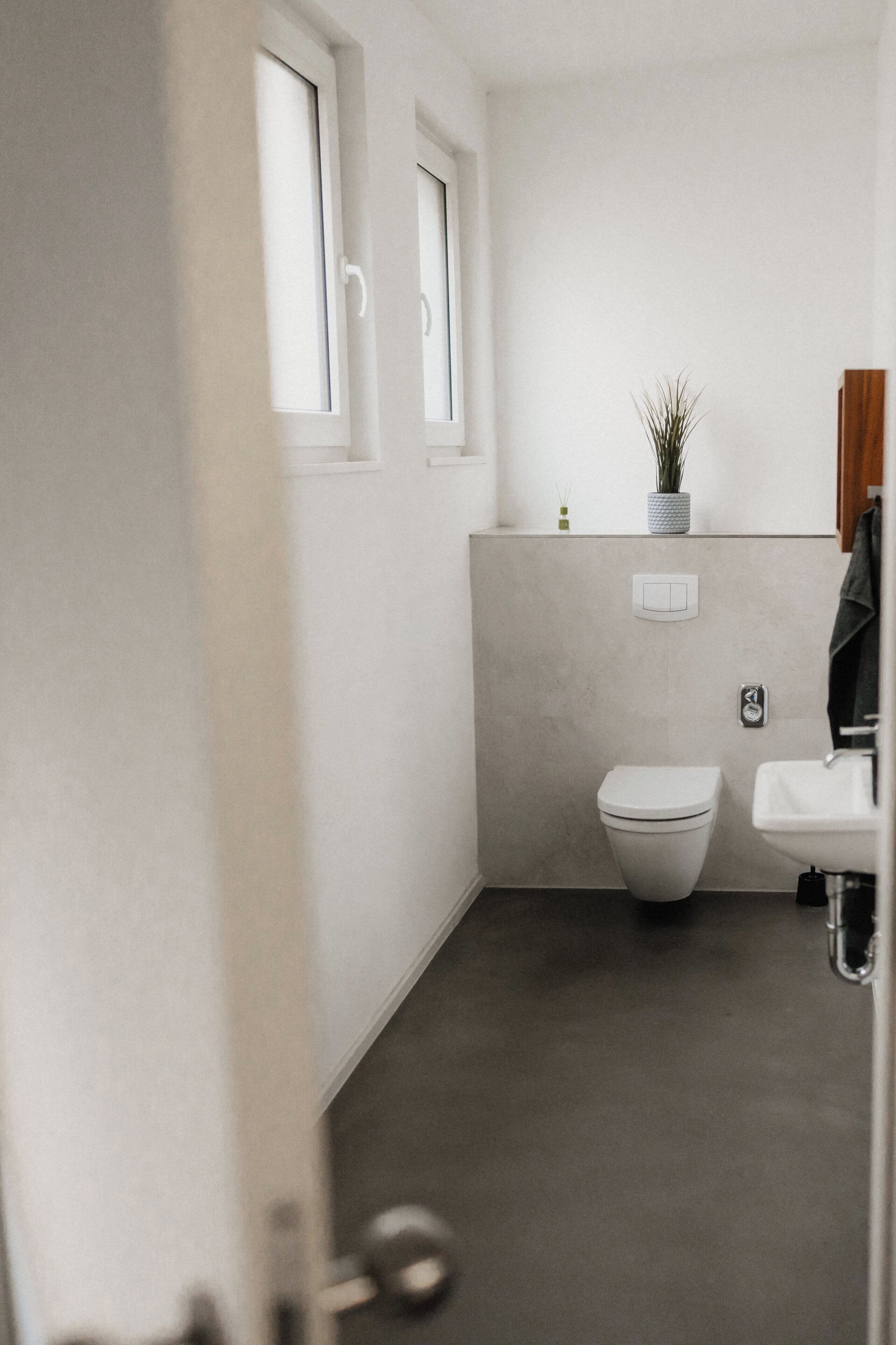 Un baño moderno con inodoro, lavamanos y una planta en maceta en la pared.