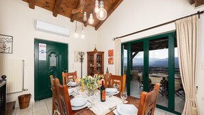 A dining area with a wooden table set for four, a green door, and a view of mountains through the open door.
