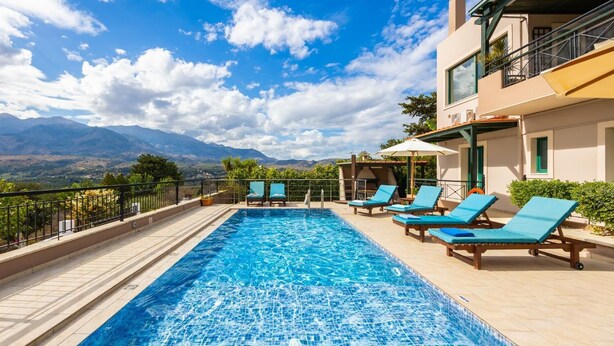A rectangular swimming pool with clear blue water, surrounded by lounge chairs and a tiled deck.