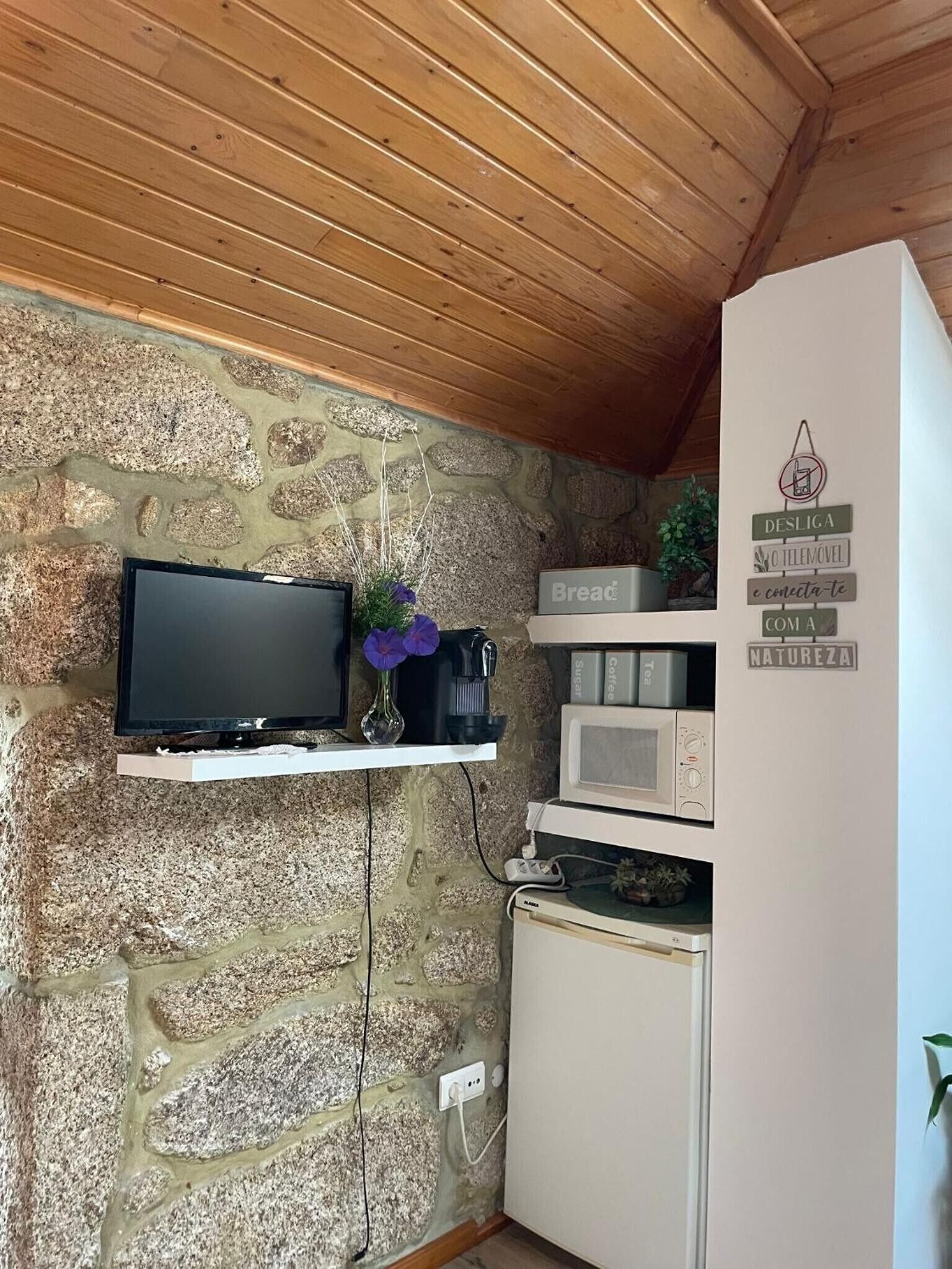 A stone wall with a mounted television, a microwave, and a refrigerator.
