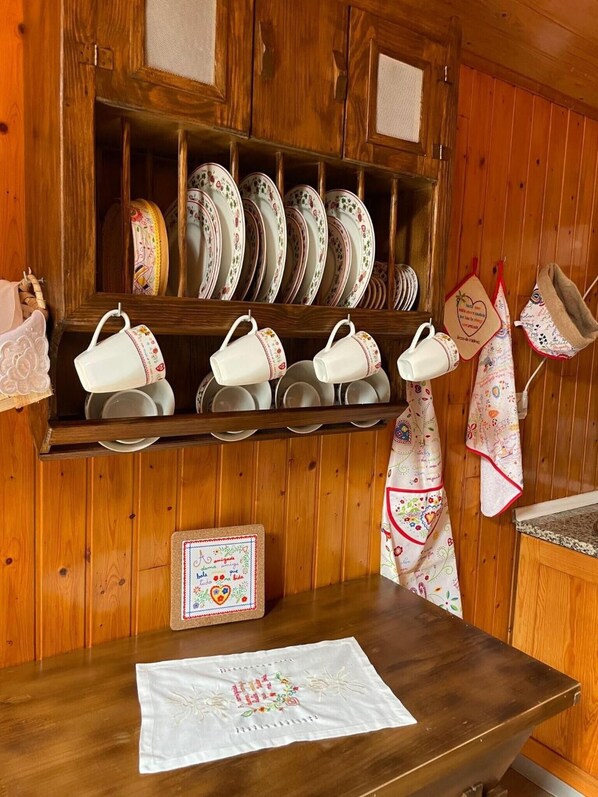 Cocina de madera con estantes que contienen platos, tazas y un paño decorativo.