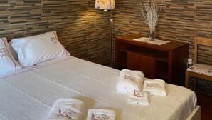 Un dormitorio con techo de madera, una cama con ropa de cama y toallas blancas, una mesita de noche con lámpara y una pared de madera.