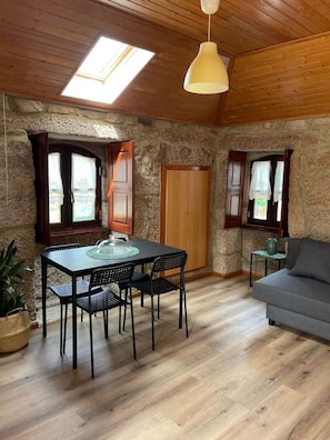 Una habitación acogedora con techo de madera, paredes de piedra, una mesa de comedor con sillas, un sofá y una pequeña mesita.