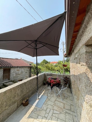 En udendørs terrasse med stenvægge, et bord, stole og en stor parasol, med udsigt til omkringliggende bygninger.