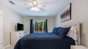 Une chambre à coucher avec un lit, une télévision, un ventilateur de plafond et une fenêtre avec des rideaux.