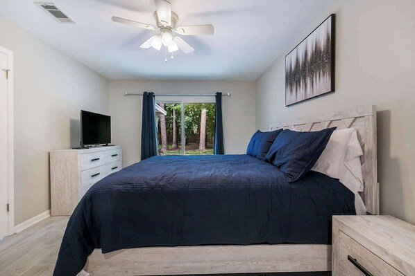 A bedroom with a bed, a TV, a ceiling fan, and a window with curtains.