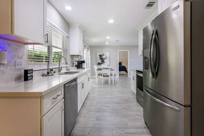 A modern kitchen with stainless steel appliances, a dining area with a table and chairs, and a view of the living area. - Charming Home (Slidell)