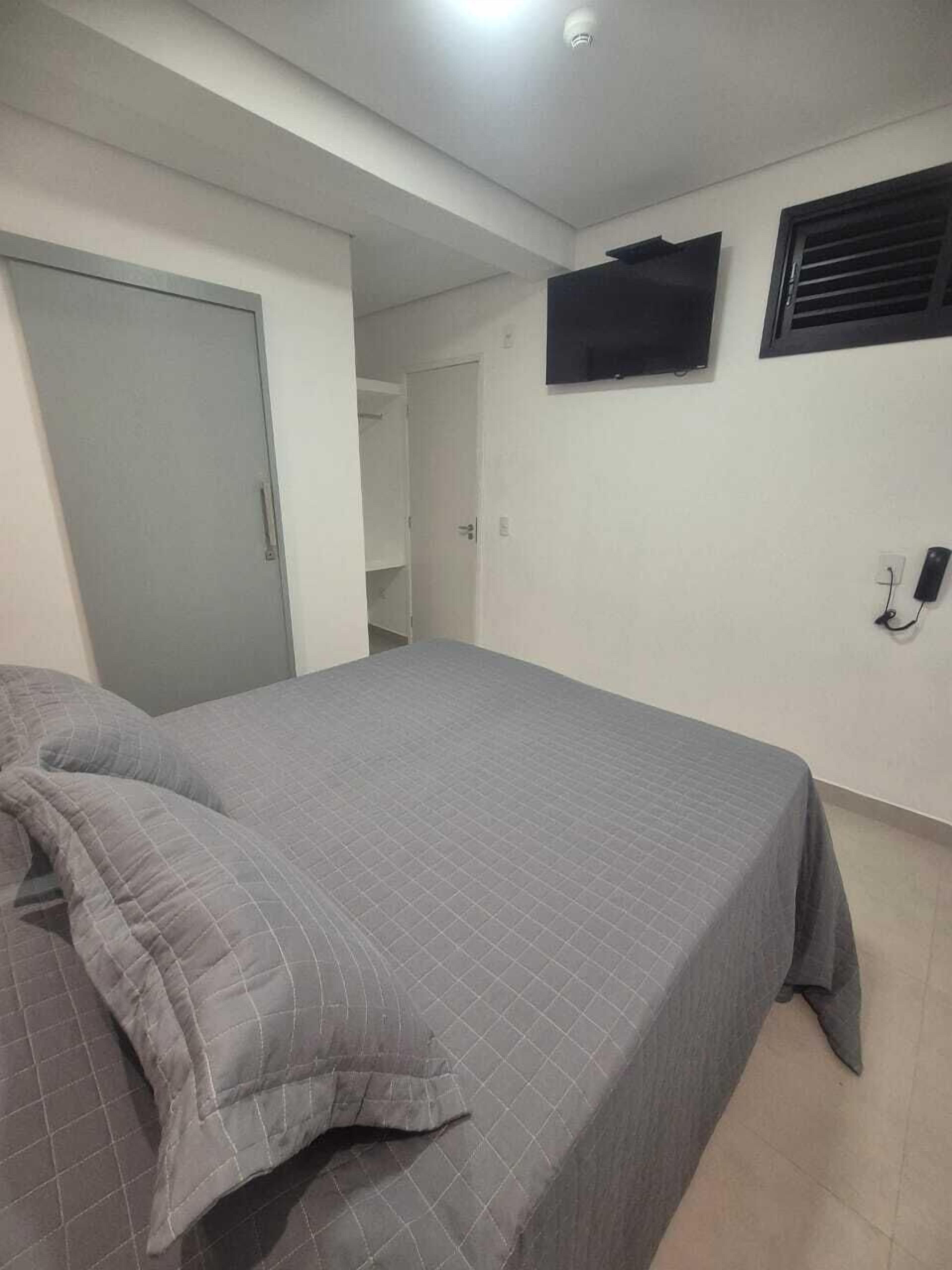 A bedroom with a bed, a TV mounted on the wall, and a door leading to another room.