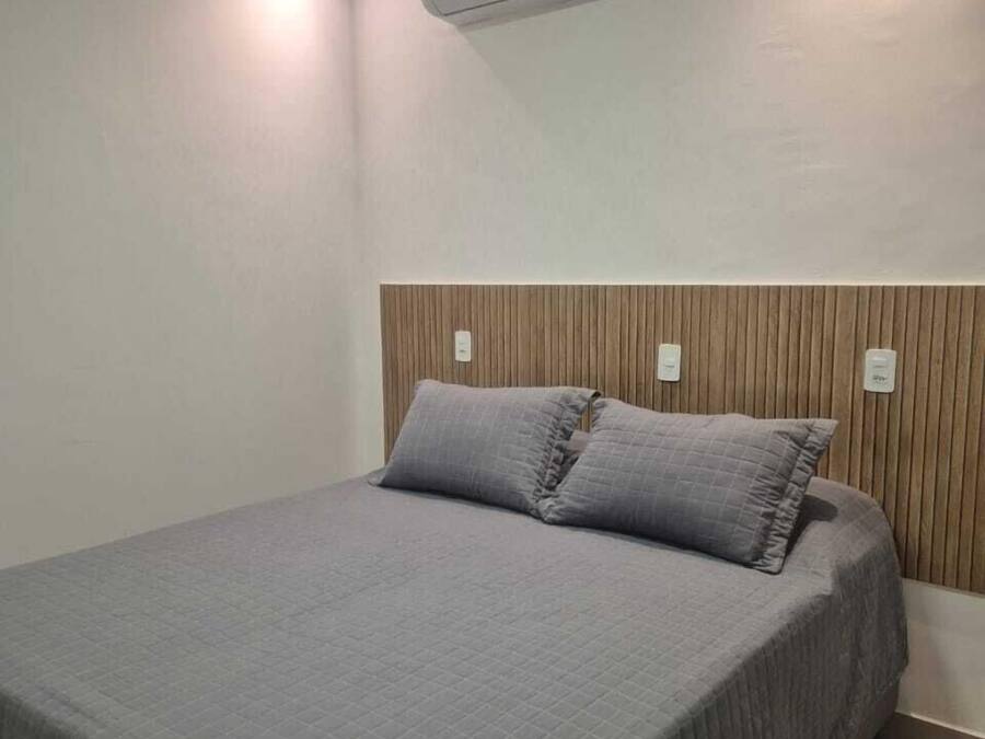 Habitación individual con una cama y cabecera de madera, ropa de cama gris y un equipo de aire acondicionado instalado en la pared.