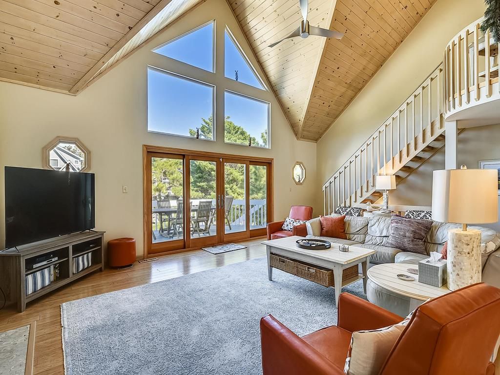 A spacious living area with a large TV, comfortable seating, a staircase, and a view through the glass doors.