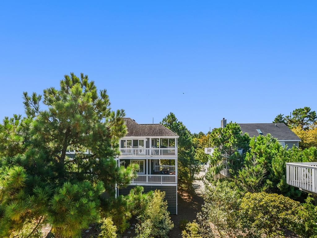 A two-story residential building with a balcony, surrounded by trees and shrubs.