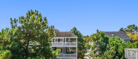 A two-story residential building with a balcony, surrounded by trees and shrubs.