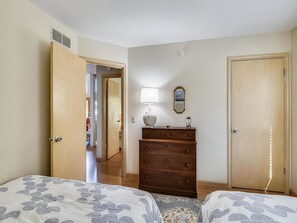Une chambre avec deux lits, une commode, une lampe et une porte.