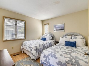 Een slaapkamer met twee bedden, een raam met zonwering, een lijst met foto aan de muur, en een klein tafeltje.