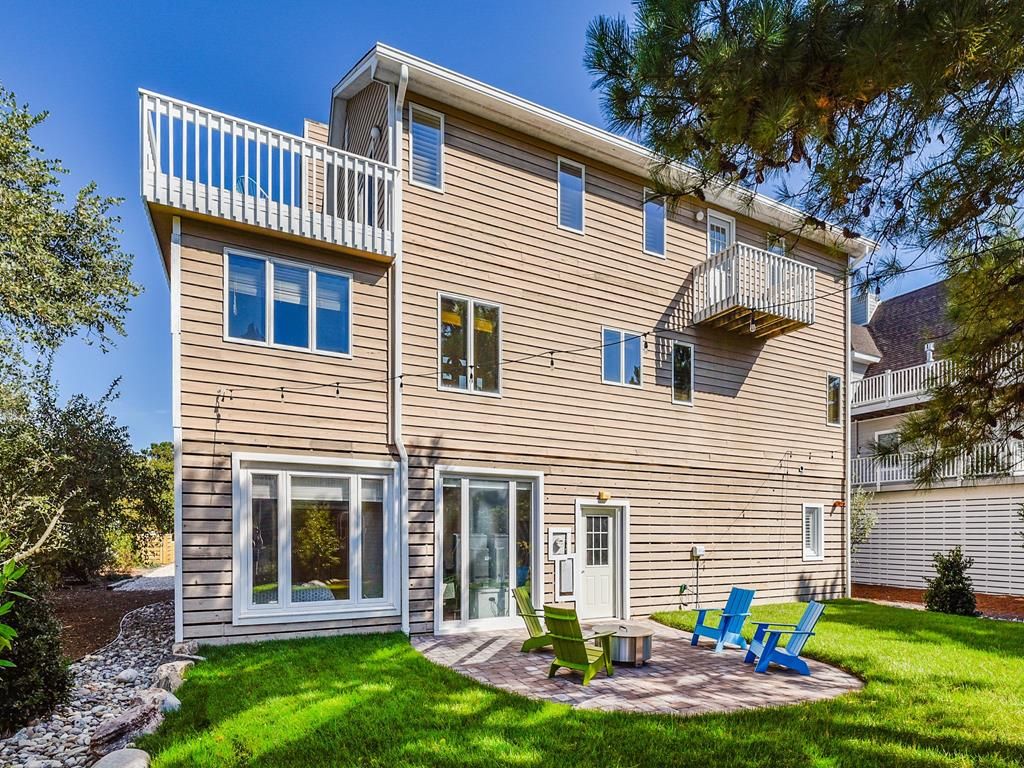 A two-story house with a balcony, a patio with outdoor furniture, and a well-maintained lawn.