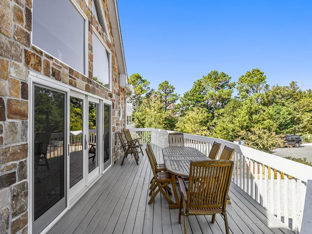 Une terrasse en bois avec une table et des chaises, une balustrade blanche et un bâtiment en pierre doté de portes vitrées.
