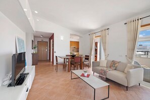 Una sala moderna con sofá, mesa de centro, televisor y comedor con sillas y mesa.