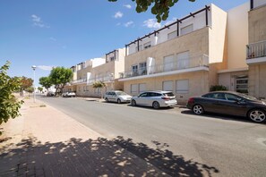 A residential street with multi-story buildings, parked cars, and a clear sky.