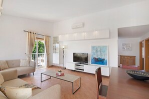 Una sala de estar con un sofá, una mesa de centro, televisión y una obra de arte en la pared.