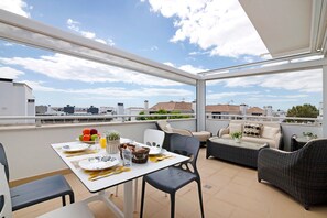 A balcony with a table set for dining, wicker furniture, and a view of the cityscape.
