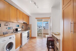 Une cuisine compacte avec des meubles en bois, un lave-linge, un grille-pain et un coin repas équipé de tabourets.