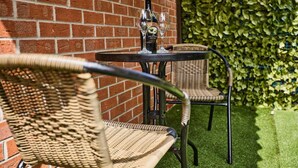 A wicker chair and table set against a brick wall with a green hedge in the background. - Ampee Guest Suite-Free Parking (Liverpool)