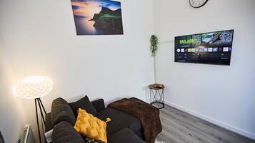 Ein modernes Wohnzimmer mit einem schwarzen Sofa, einer Lampe, einem Wand-Fernseher und einem Gemälde einer Abendlandschaft.