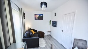 A modern living room with a sofa, a small side table, a white door, and a chandelier. - Ampee Guest Suite-Free Parking (Liverpool)