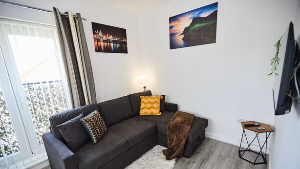 Una sala de estar moderna con un sofá seccional gris oscuro, una alfombra blanca y mullida, y dos cuadros colgados en la pared.