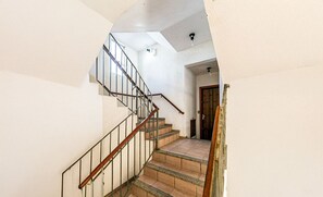 A staircase with a wooden handrail and metal balusters, leading to a room with a wooden door and a light fixture on the ceiling.