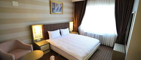 A hotel room with a large bed, two bedside tables with lamps, a chair, and a window with curtains.
