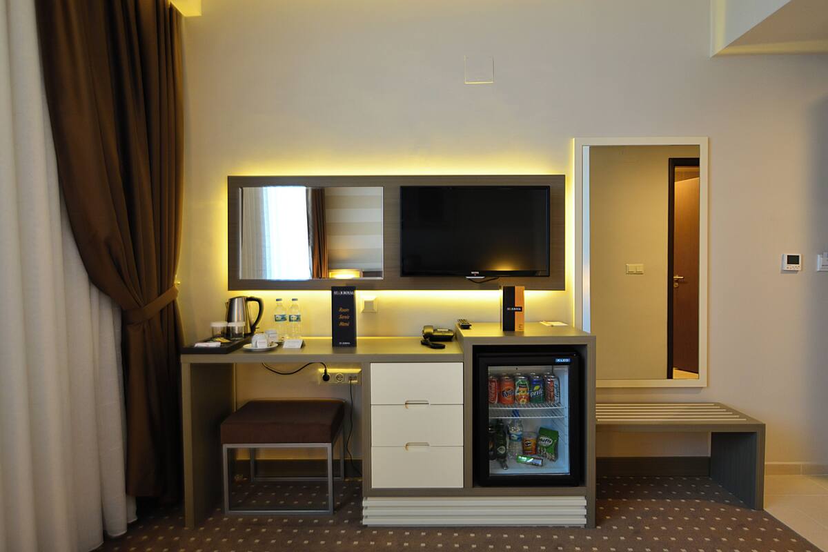 A compact hotel room with a kitchenette, a television, a mini-fridge, a small seating area, and a door leading to the bathroom.