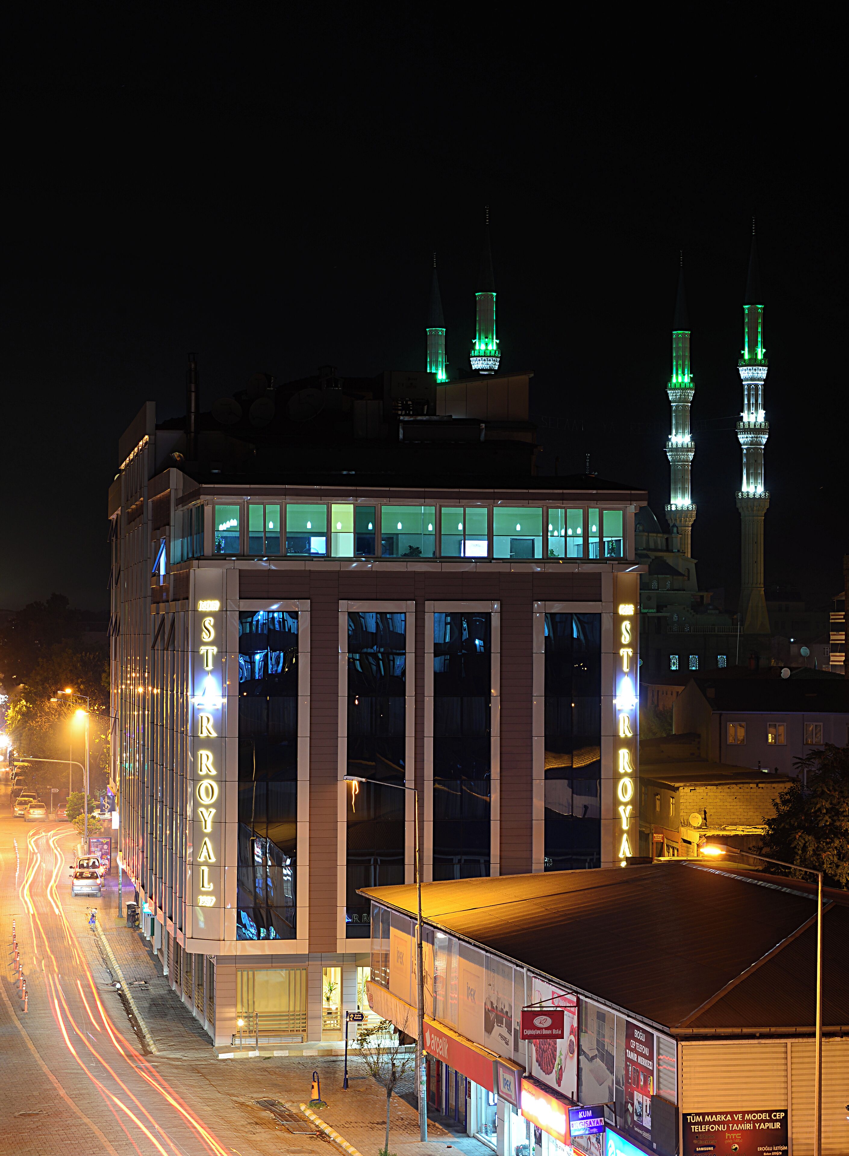 Ein modernes Gebäude mit beleuchteter Beschilderung, einem markanten Eingang und Blick auf nahegelegene Minarette.