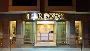 The exterior of a hotel named "Star Royal" with a prominent illuminated sign, large glass entrance, and potted plants on either side.