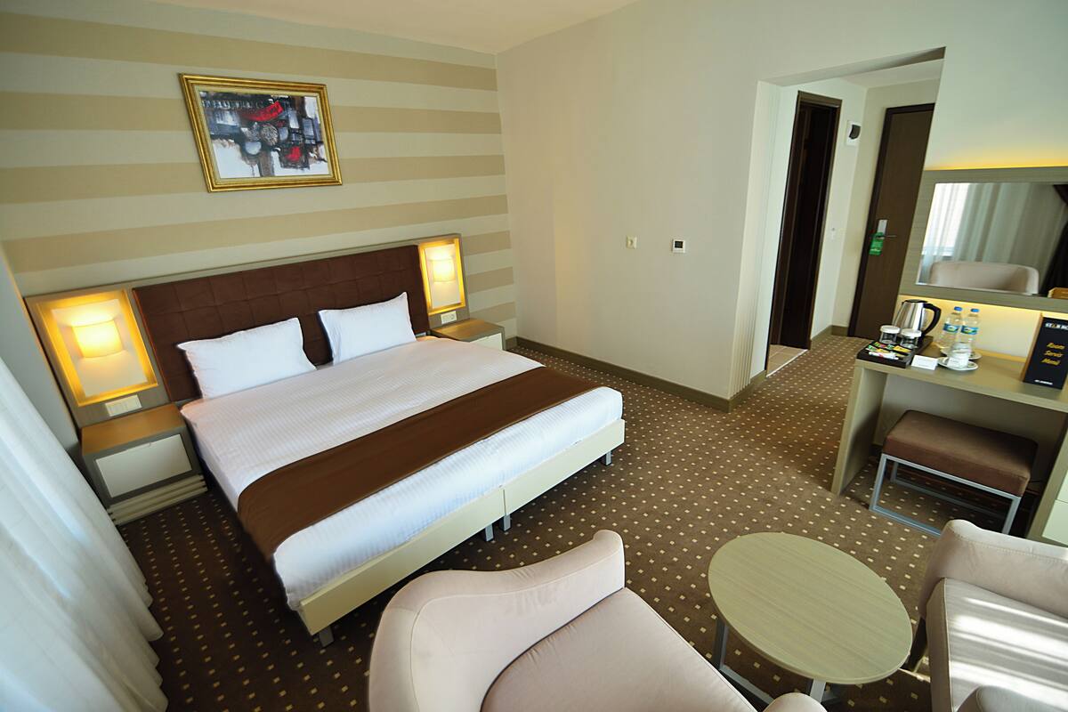 A hotel room with a large bed, bedside lamps, a desk with a chair, a small round table, and a mirror.