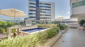 A rooftop pool area with a blue pool, surrounded by potted plants and umbrellas. - Apt With River View and Balcony Pontal Bcl402 (Ilhéus)