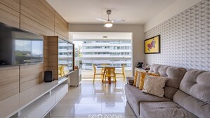Un salon moderne doté d’un téléviseur à écran plat, d’un canapé, d’un coin repas avec des chaises et d’un balcon offrant une vue sur les bâtiments.