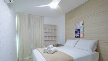 Une chambre d’hôtel comprenant un lit, une table de chevet, une étagère fixée au mur et un ventilateur de plafond.