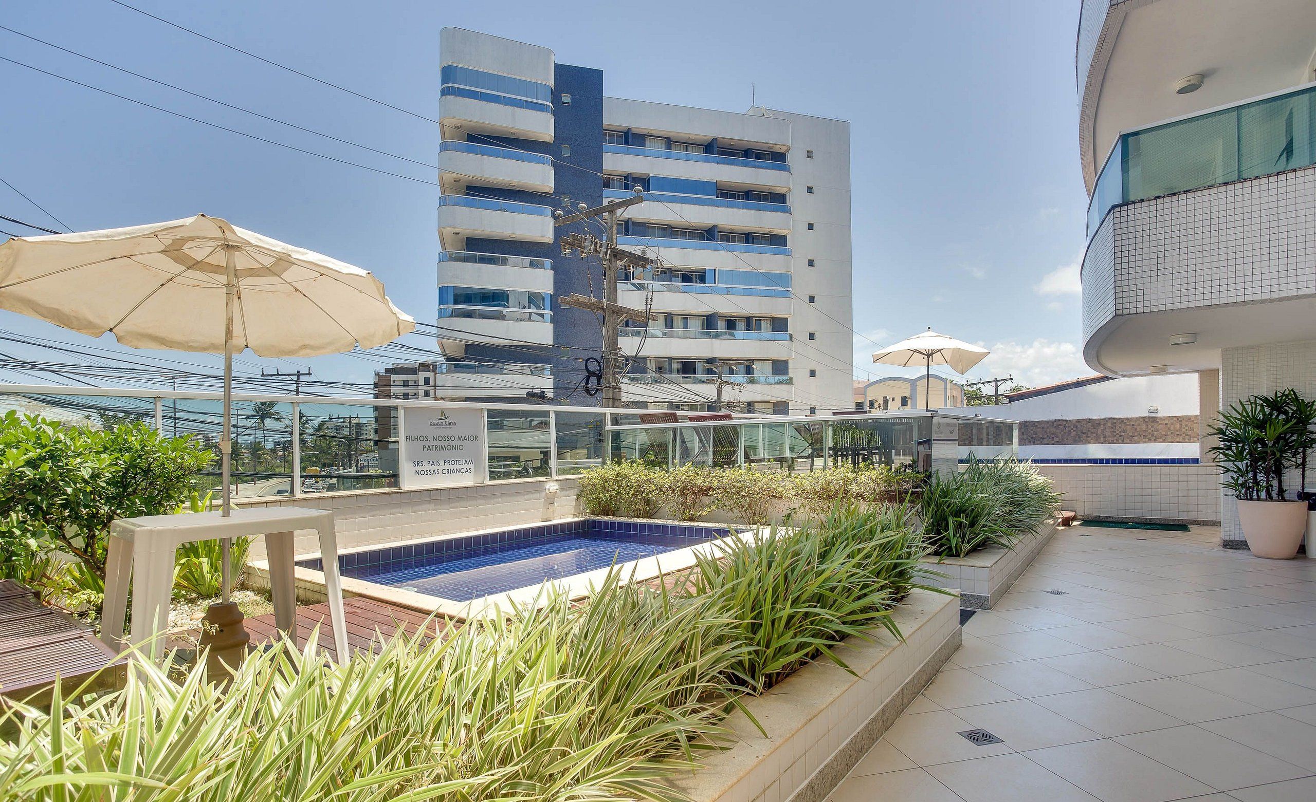 A rooftop pool area with a blue pool, surrounded by potted plants and umbrellas.