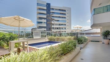 A rooftop pool area with a blue pool, surrounded by potted plants and umbrellas.
