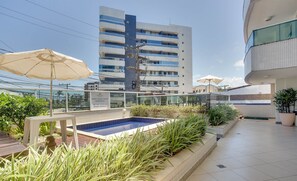 Un área de piscina en la azotea con piscina azul, rodeada de macetas y sombrillas.