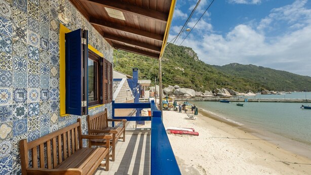 Un edificio sul lungomare con rivestimento in piastrelle, panche di legno e vista sulla spiaggia e sulle montagne.
