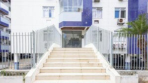 A building with a white facade and blue-tiled upper section, featuring a staircase leading to a glass door entrance. - Confort y Estilo en Itacorubi, Floripa Apc0207 (Florianópolis)